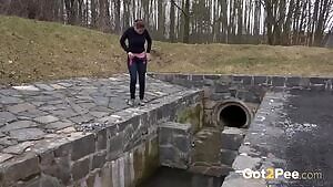 Brunette sprays her piss over the edge of a public drainage pipe